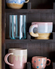 Collection of ceramic mugs with gradient designs on a wooden shelf.
