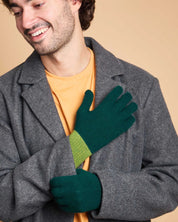A man wearing a gray wool coat over a yellow-orange t-shirt, showcasing a pair of dark green knit gloves with a lime green ribbed cuff.