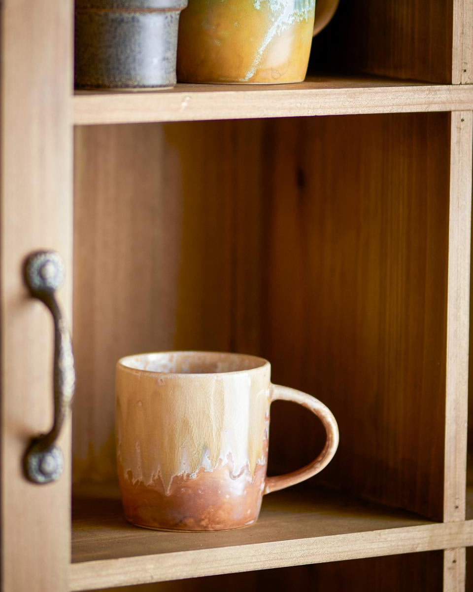 Ceramic mug on a wooden shelf with a rustic cabinet.