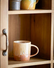 Ceramic mug on a wooden shelf with a rustic cabinet.