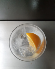 A gin and tonic cocktail in a glass with ice cubes and a piece of orange