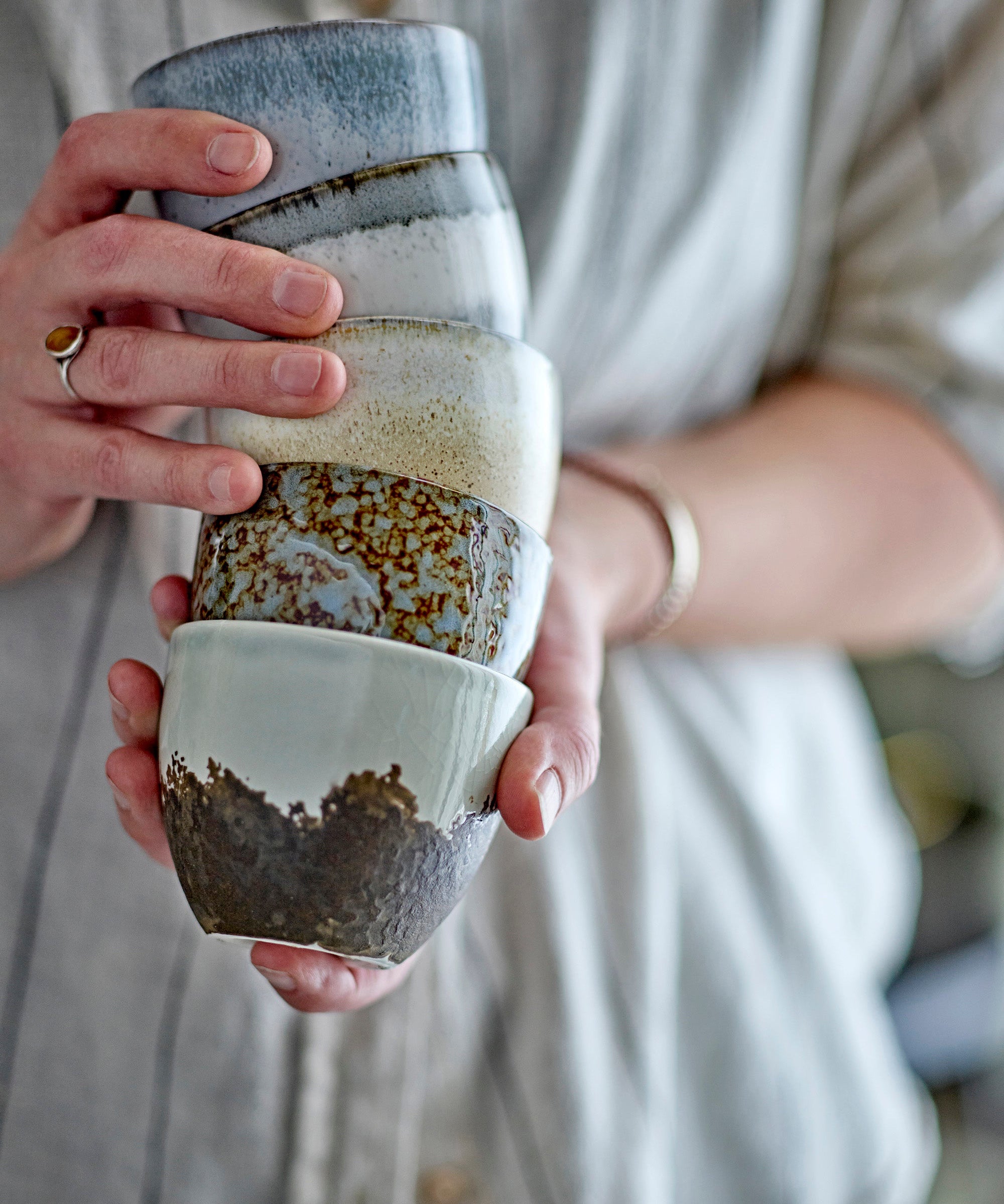 Person holding a stack of ceramic cups with layered textures and colors.