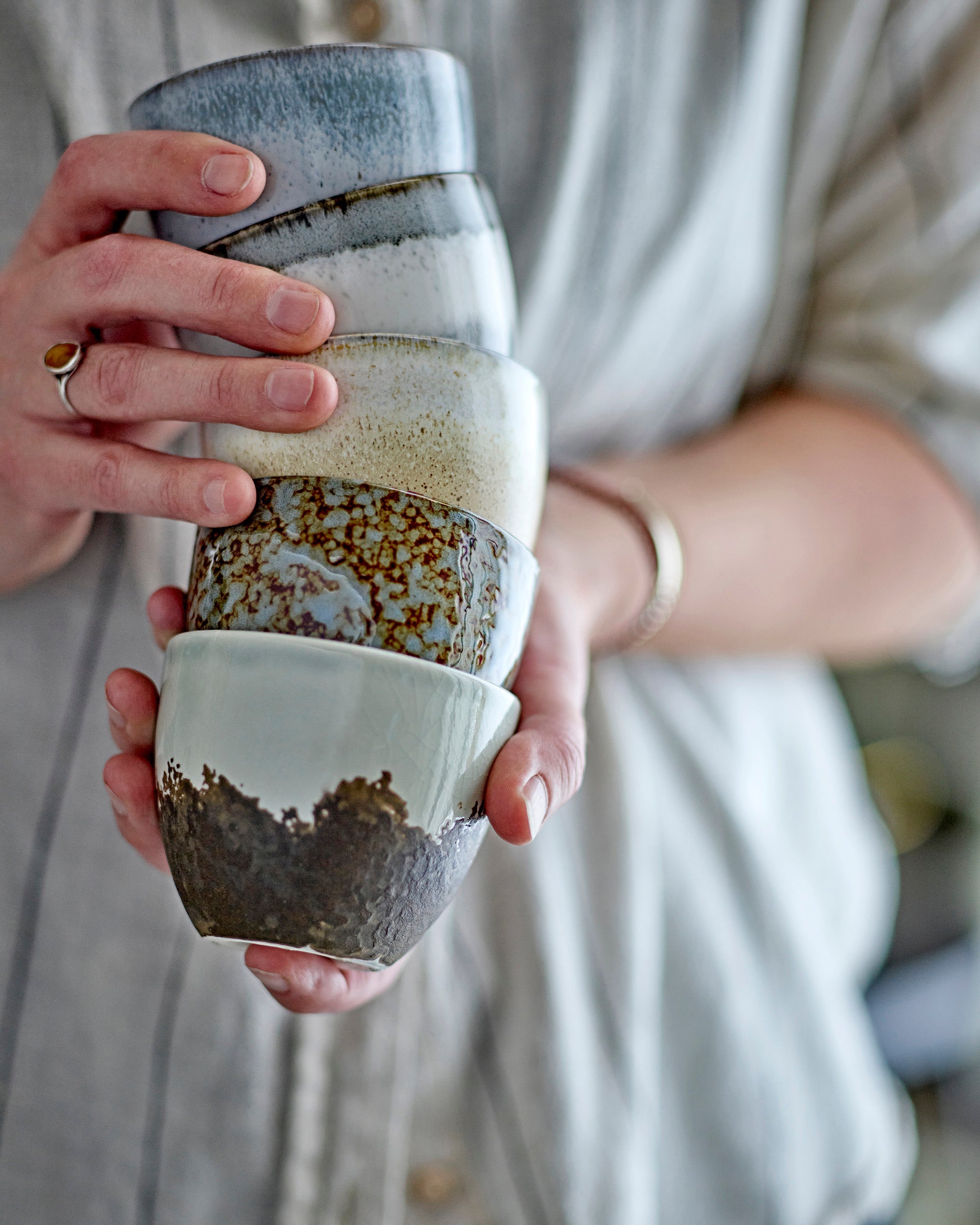 Person holding a stack of ceramic cups with layered textures and colors.