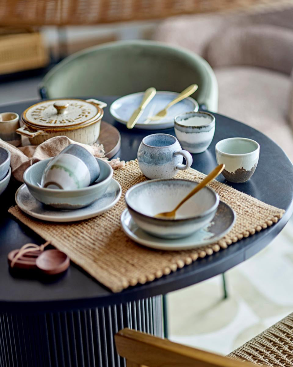Ceramic dishes on a round table with woven placemats and wooden spoons.