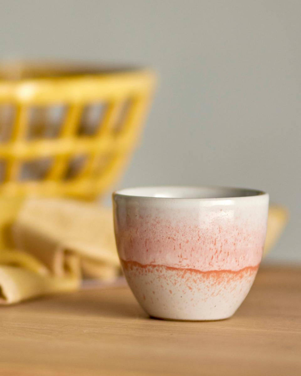 Ceramic cup with gradient design on a wooden surface with a blurred yellow basket in the background