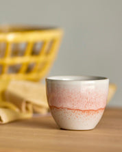 Ceramic cup with gradient design on a wooden surface with a blurred yellow basket in the background