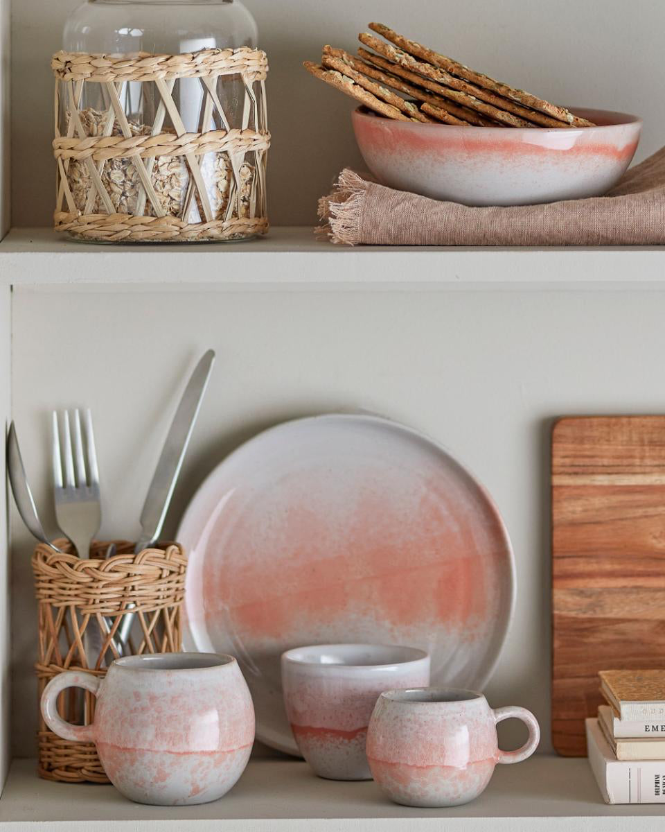 Ceramic plates, mugs, and cutlery on a shelf with a wooden cutting board and woven baskets.