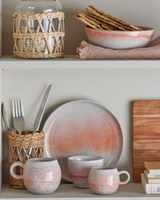 Ceramic plates, mugs, and cutlery on a shelf with a wooden cutting board and woven baskets.