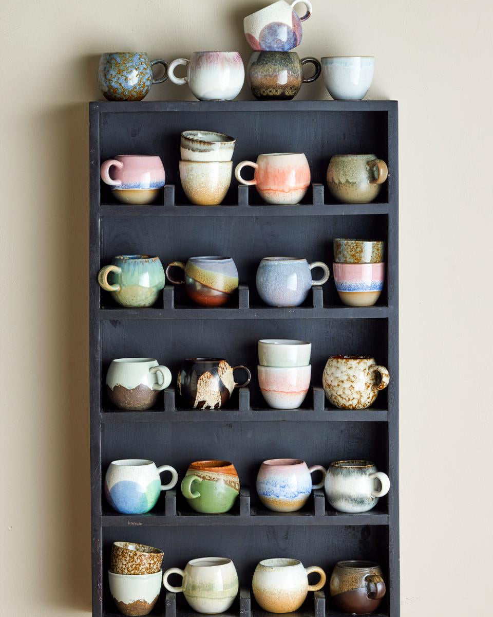 Collection of ceramic mugs on a dark wooden shelf against a beige wall.