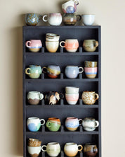 Collection of ceramic mugs on a dark wooden shelf against a beige wall.