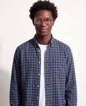 Man wearing a blue plaid shirt over a white shirt on a plain background