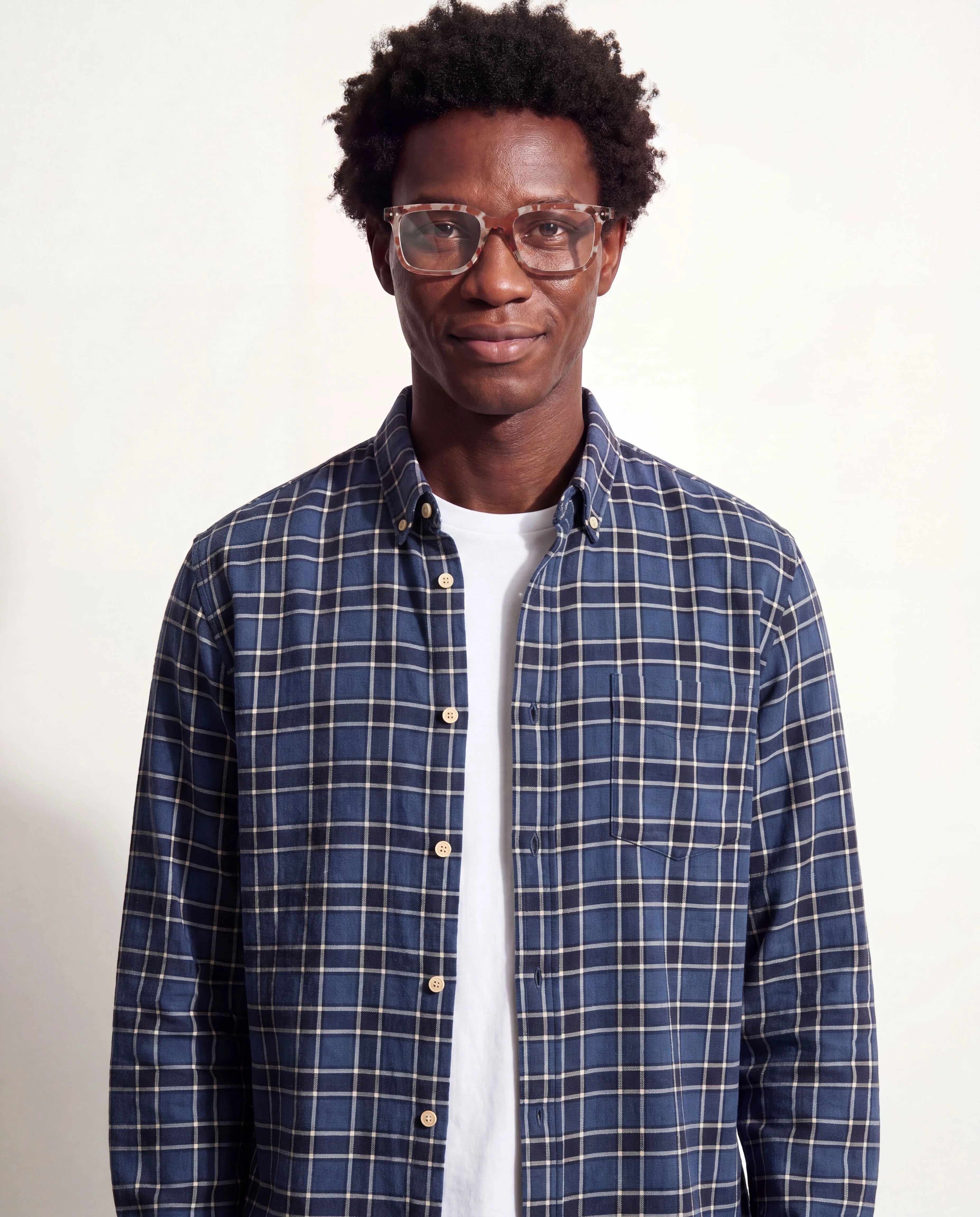 Man wearing a blue plaid shirt over a white shirt on a plain background