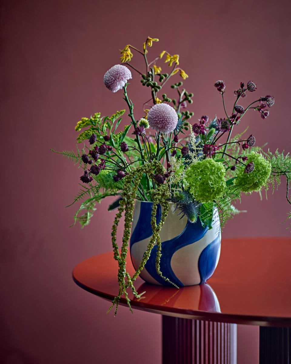 Bouquet of flowers in a blue and white vase on a red table against a pink wall