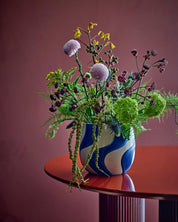 Bouquet of flowers in a blue and white vase on a red table against a pink wall