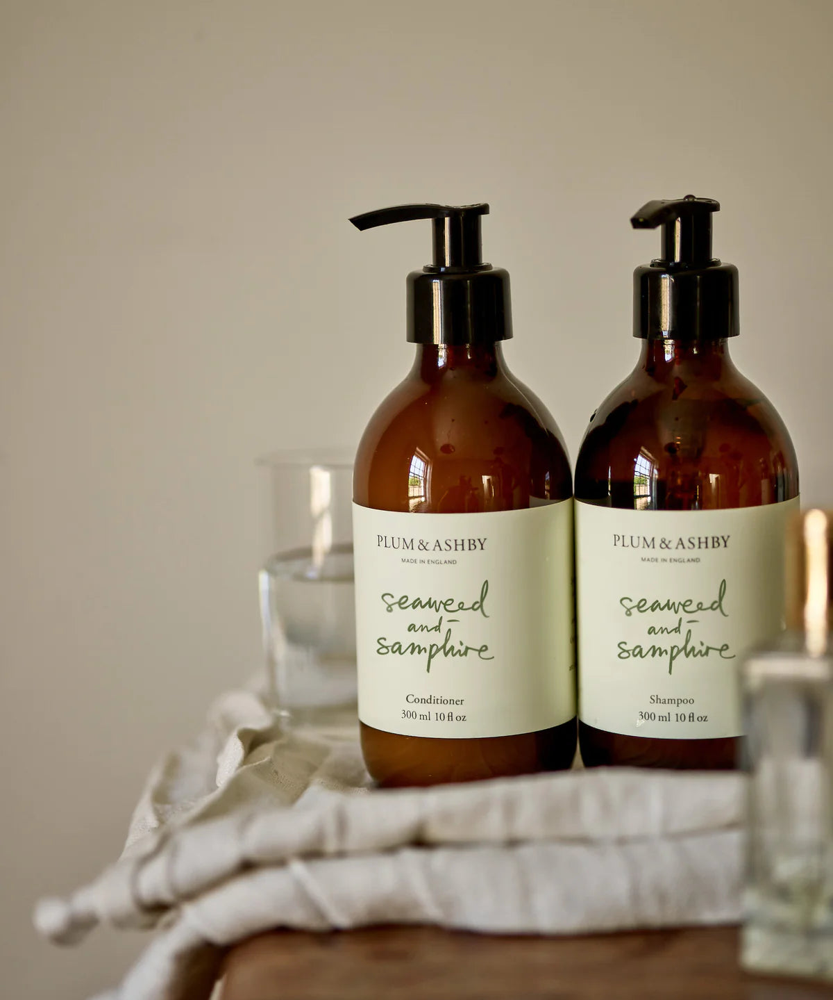 Two dark brown glass bottles, black pump dispensers, white labels with sage green writing, seaweed and samphire shampoo and conditioner by Plum and Ashby