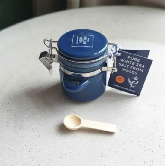 Small blue ceramic jar with a tiny wooden spoon, containing pure white sea salt from Whales by brand Halen Môn