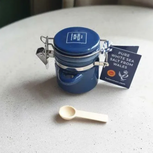 Small blue ceramic jar with a tiny wooden spoon, containing pure white sea salt from Whales by brand Halen Môn