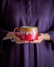 Person holding a red mug with artistic design against a purple background