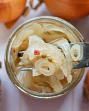 Jar of pickled onions with a fork holding some onions above the jar, surrounded by whole onions.