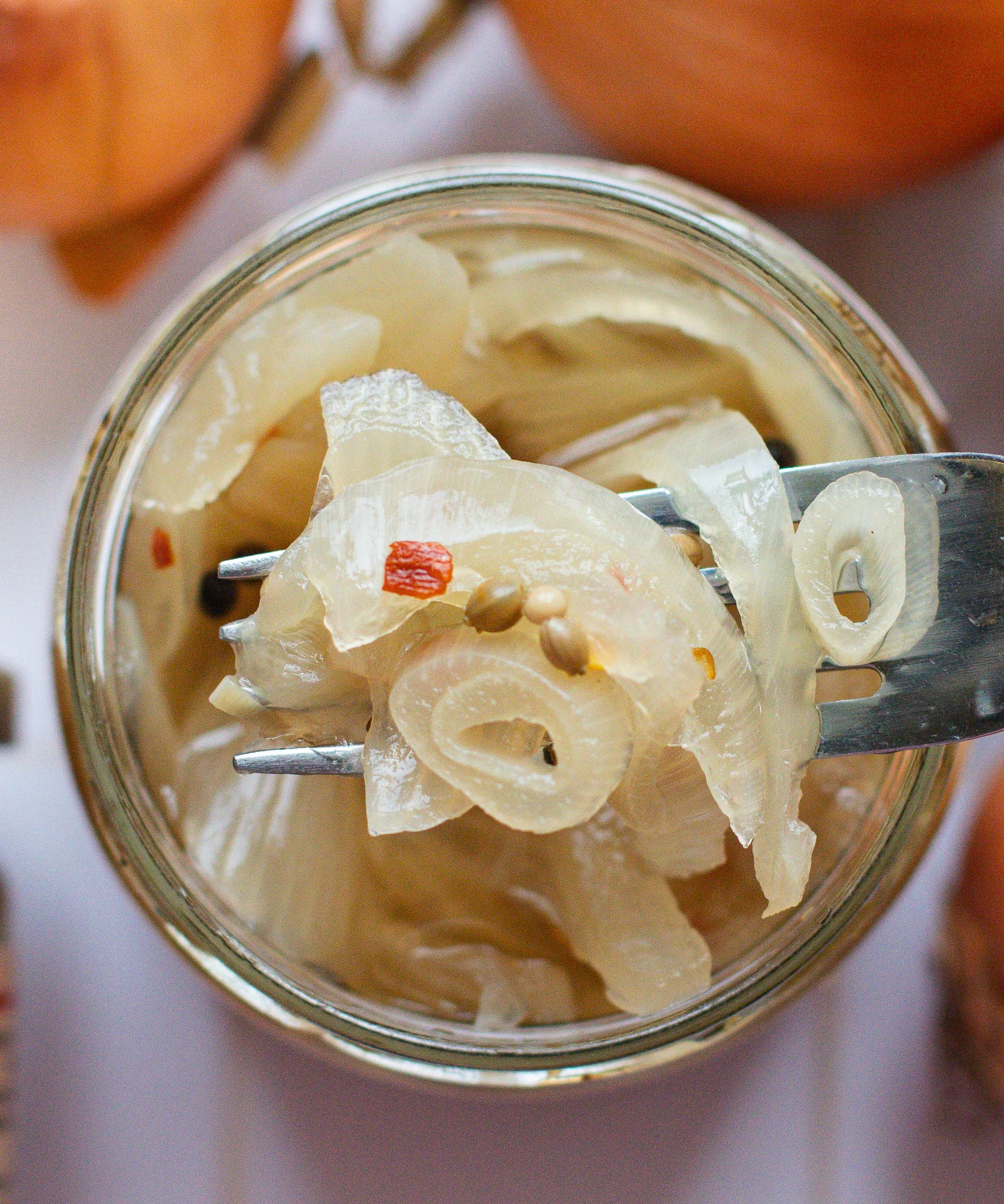 Jar of pickled onions with a fork holding some onions above the jar, surrounded by whole onions.