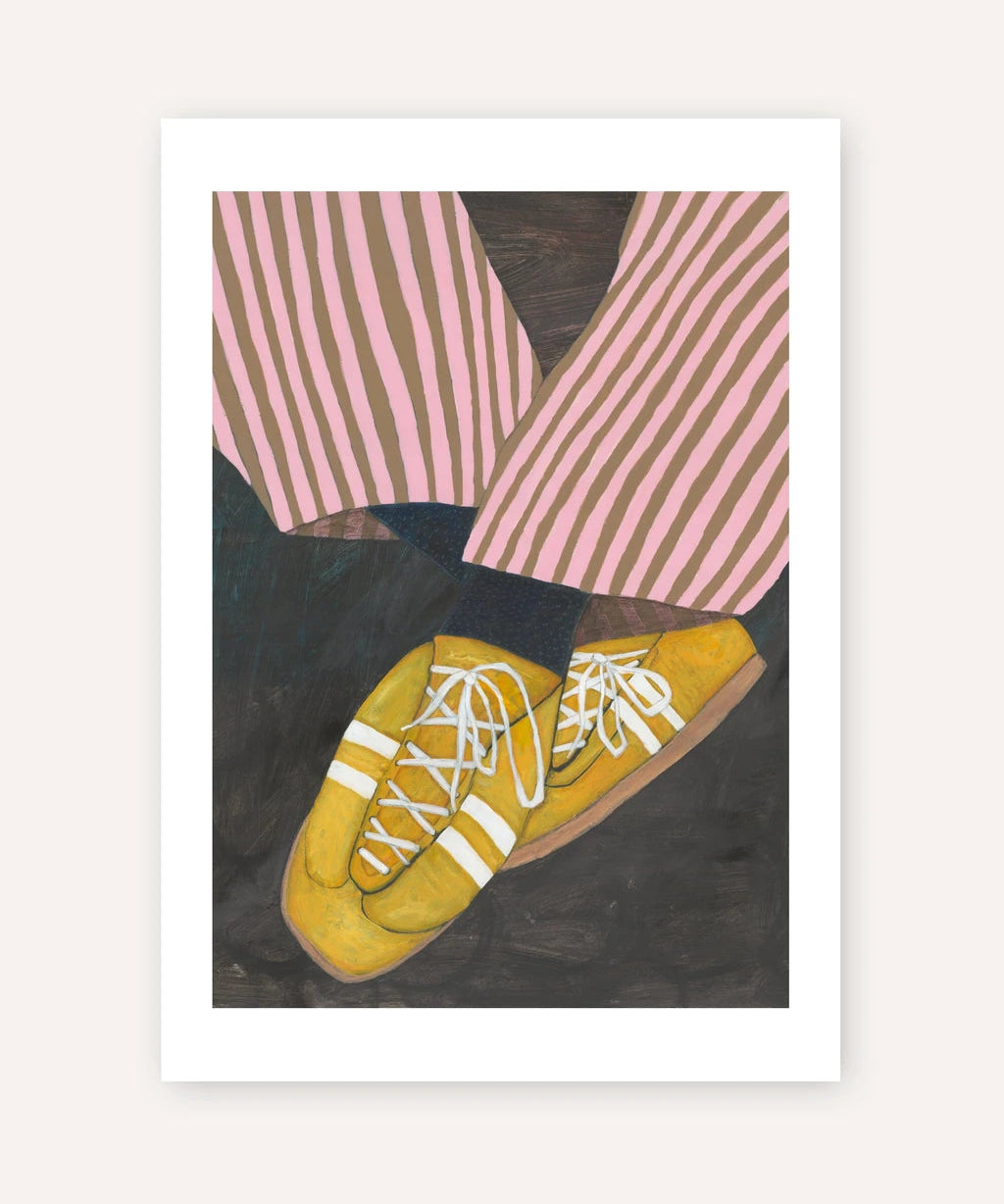 A framed art print featuring a stylized illustration of yellow sneakers with white laces, pink and brown striped trousers, and a dark background, displayed against a light beige wall.