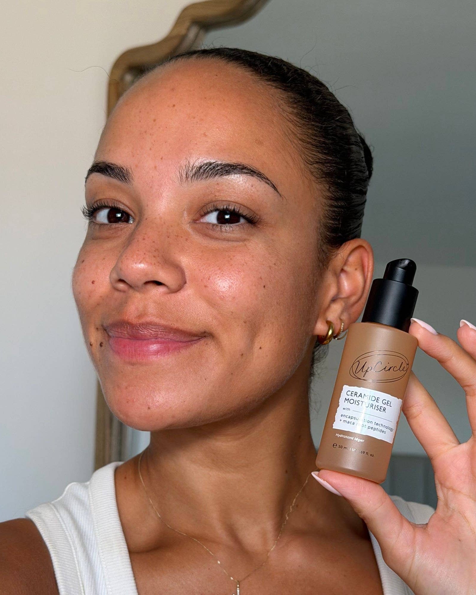 A woman holding a bottle of Ceramide Gel Moisturiser highlighted next to her face, showing the product in a lifestyle setting.