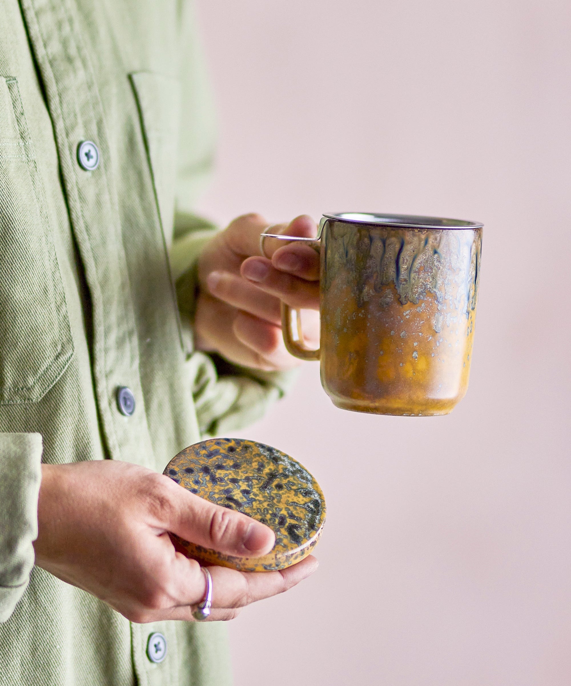 Person holding a ceramic mug and lid against a plain background
