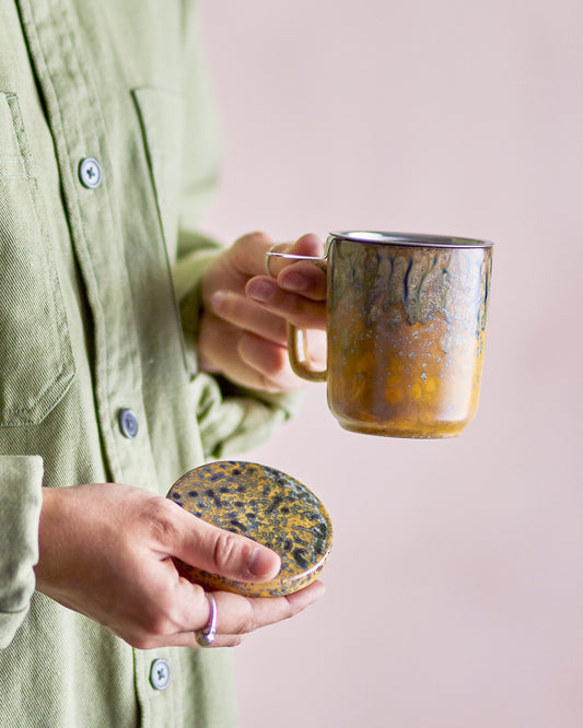 Person holding a ceramic mug and lid against a plain background