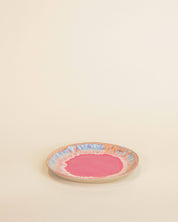 Small round ceramic plate with a pink center and colorful rim on a beige background