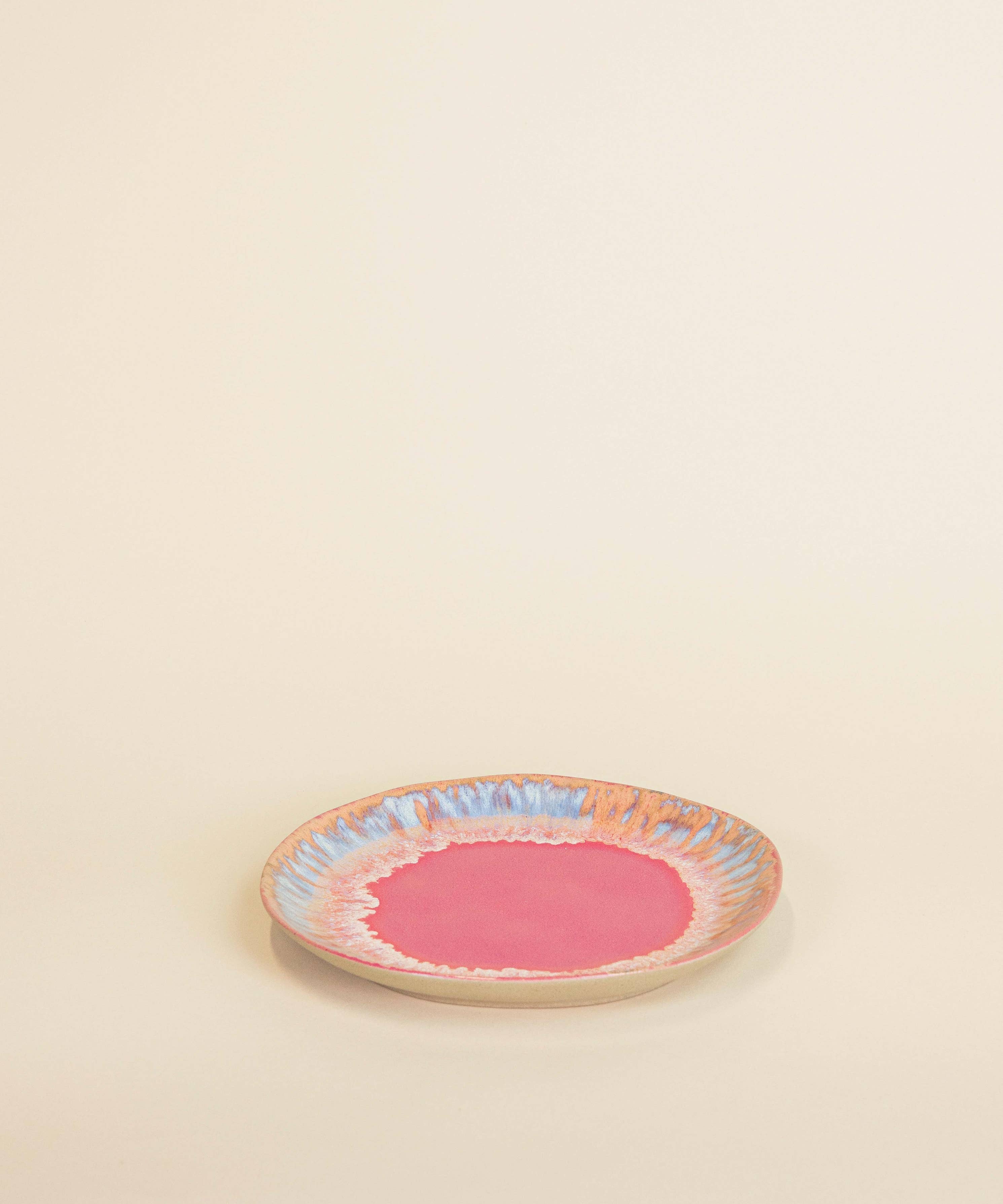 Small round ceramic plate with a pink center and colorful rim on a beige background