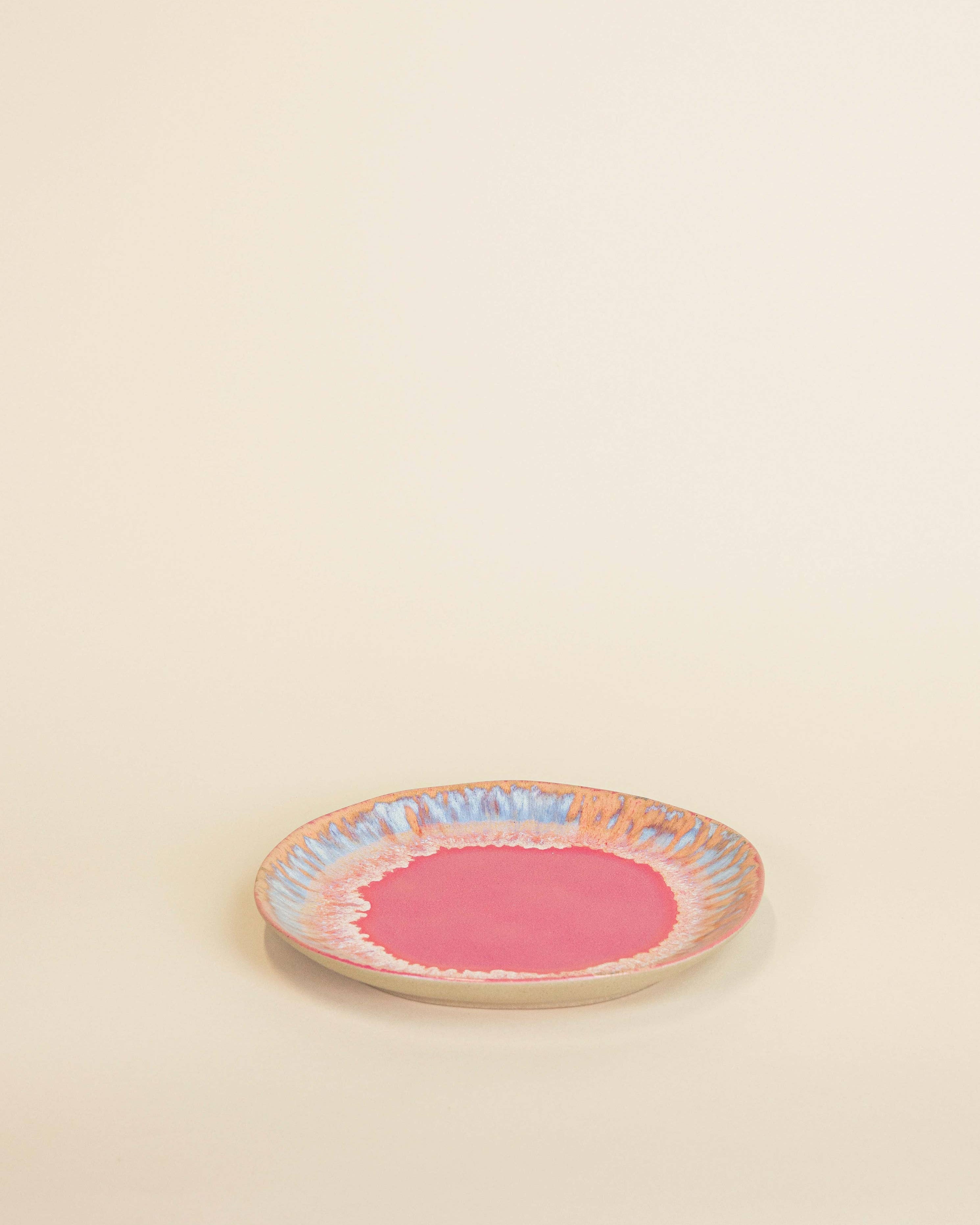 Small round ceramic plate with a pink center and colorful rim on a beige background