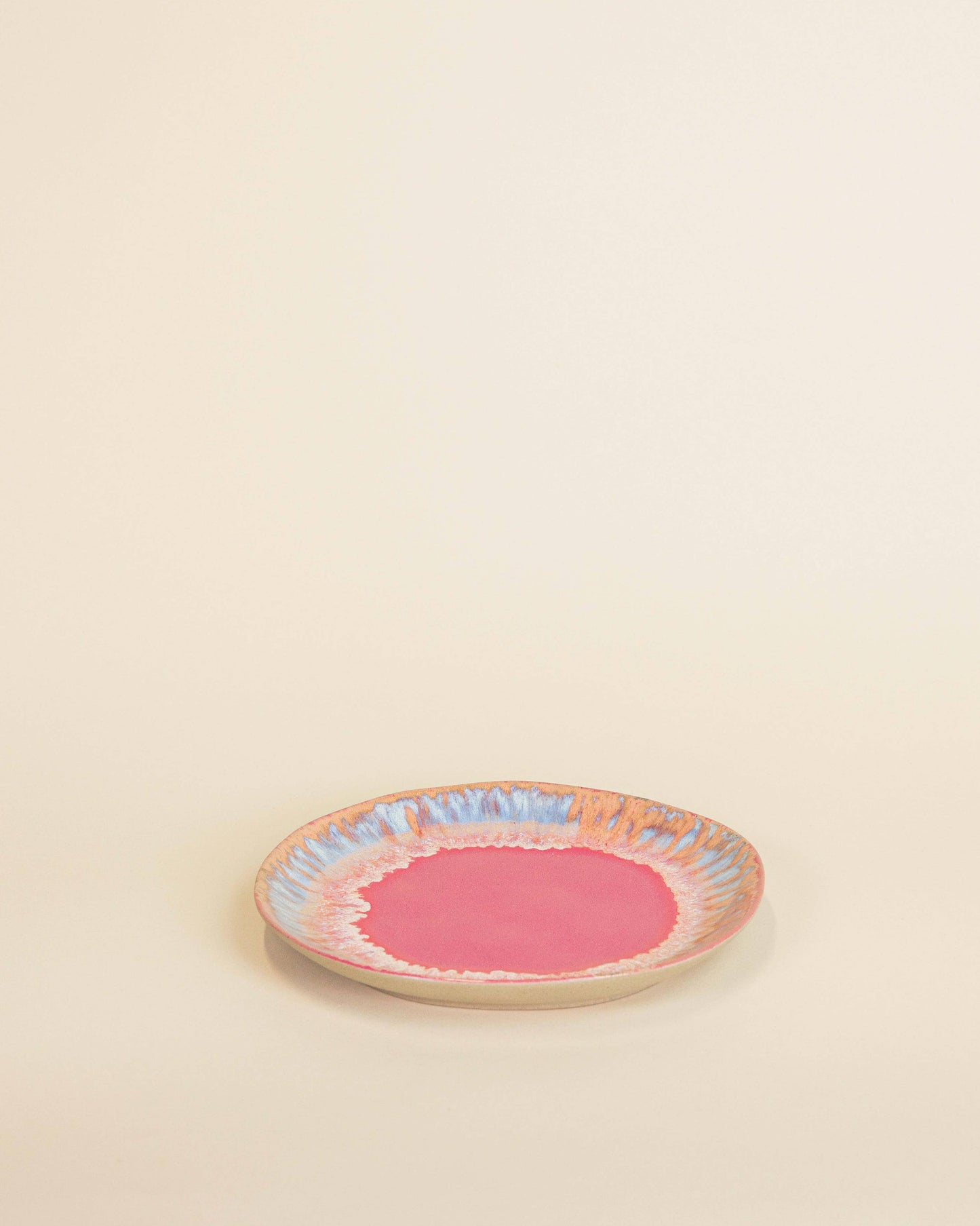 Small round ceramic plate with a pink center and colorful rim on a beige background
