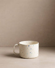 Egg Back Home white ceramic mug with colourful speckles on a beige background