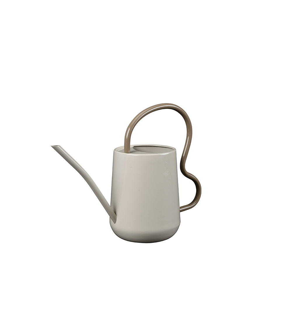 A matte off-white ceramic watering can with a long, slender spout and a sculptural, curved metallic handle in a warm bronze finish, shown against a solid white background.
