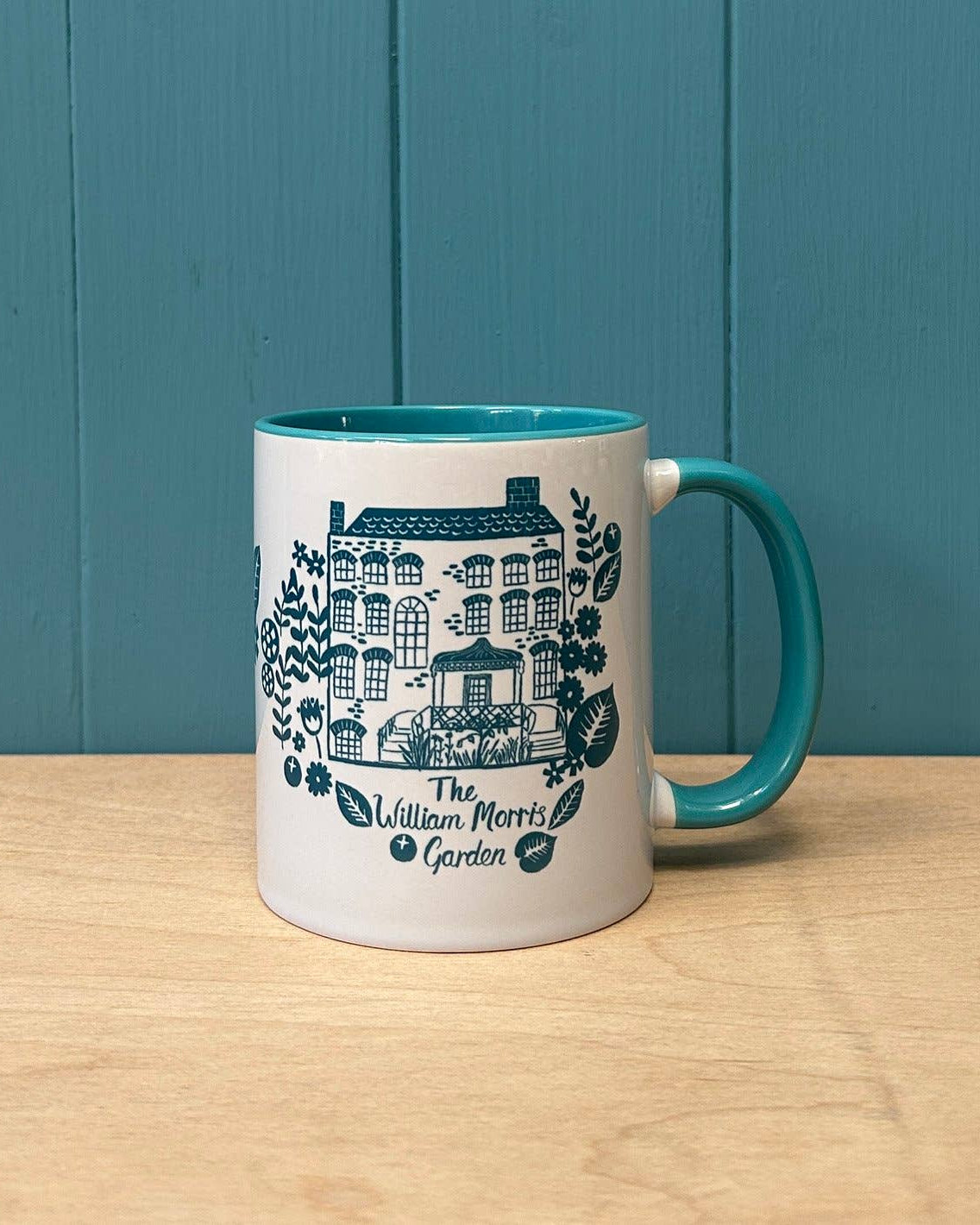 White mug with blue handle featuring a design and text on a wooden surface with a blue wall background