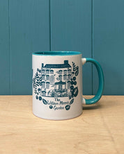White mug with blue handle featuring a design and text on a wooden surface with a blue wall background