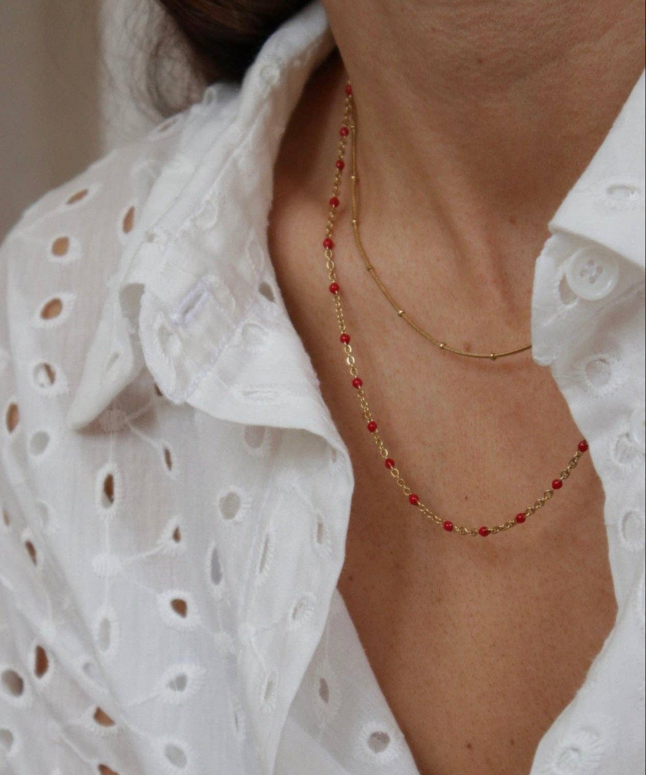 Person wearing a white lace top with a gold and red beaded necklace.