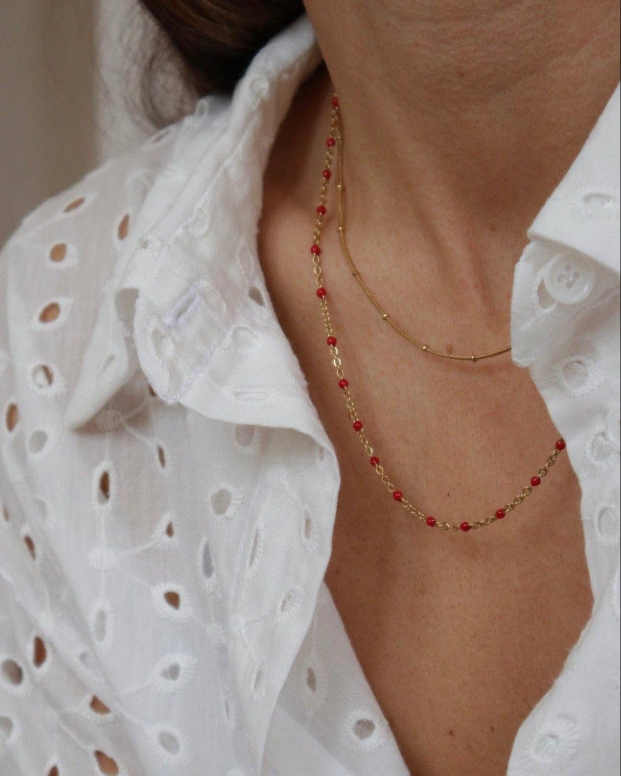 Person wearing a white lace top with a gold and red beaded necklace.
