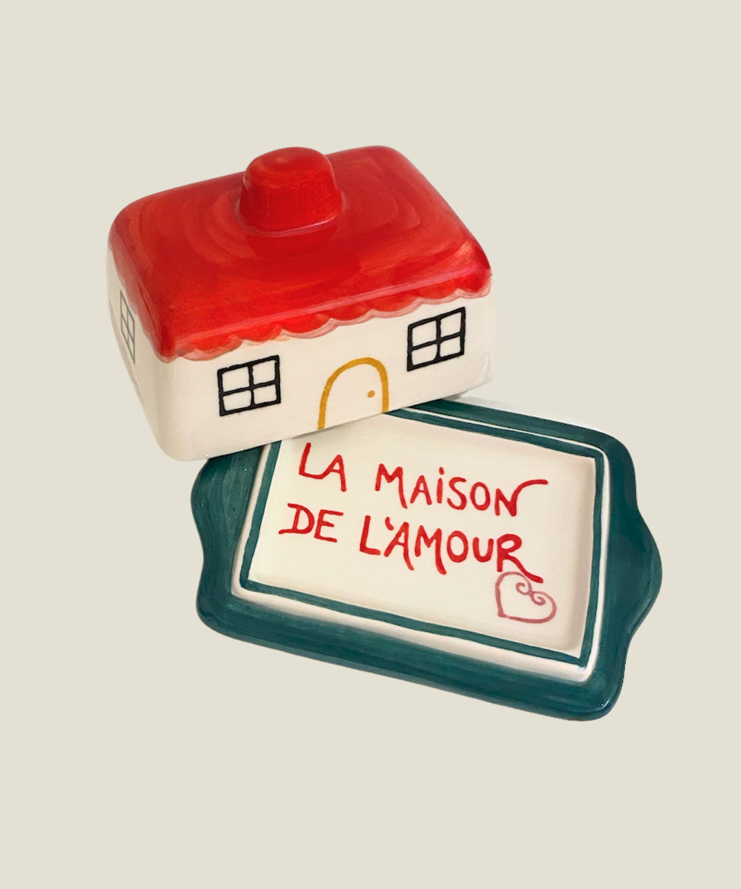 Ceramic house-shaped container with a smaller rectangular dish below on a beige background
