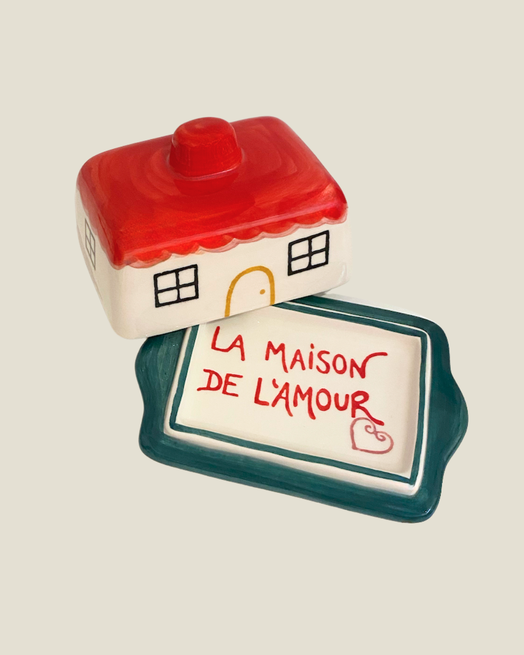 Ceramic house-shaped container with a smaller rectangular dish below on a beige background