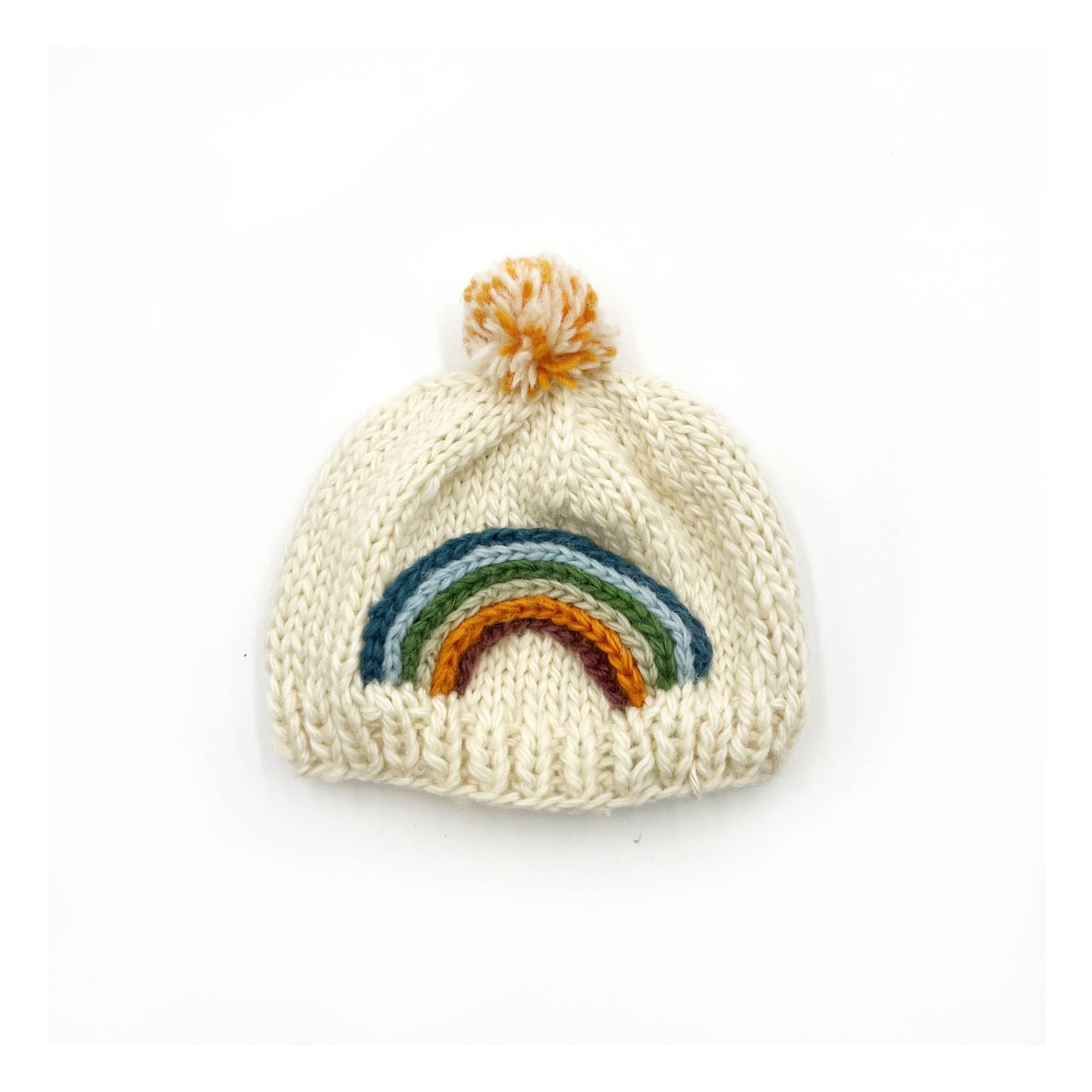 Thick, chunky woollen baby winter hat, by Pebble Child, made from 100% New Zealand merino wool in cream colour, with a knitted rainbow and a pompom on top.