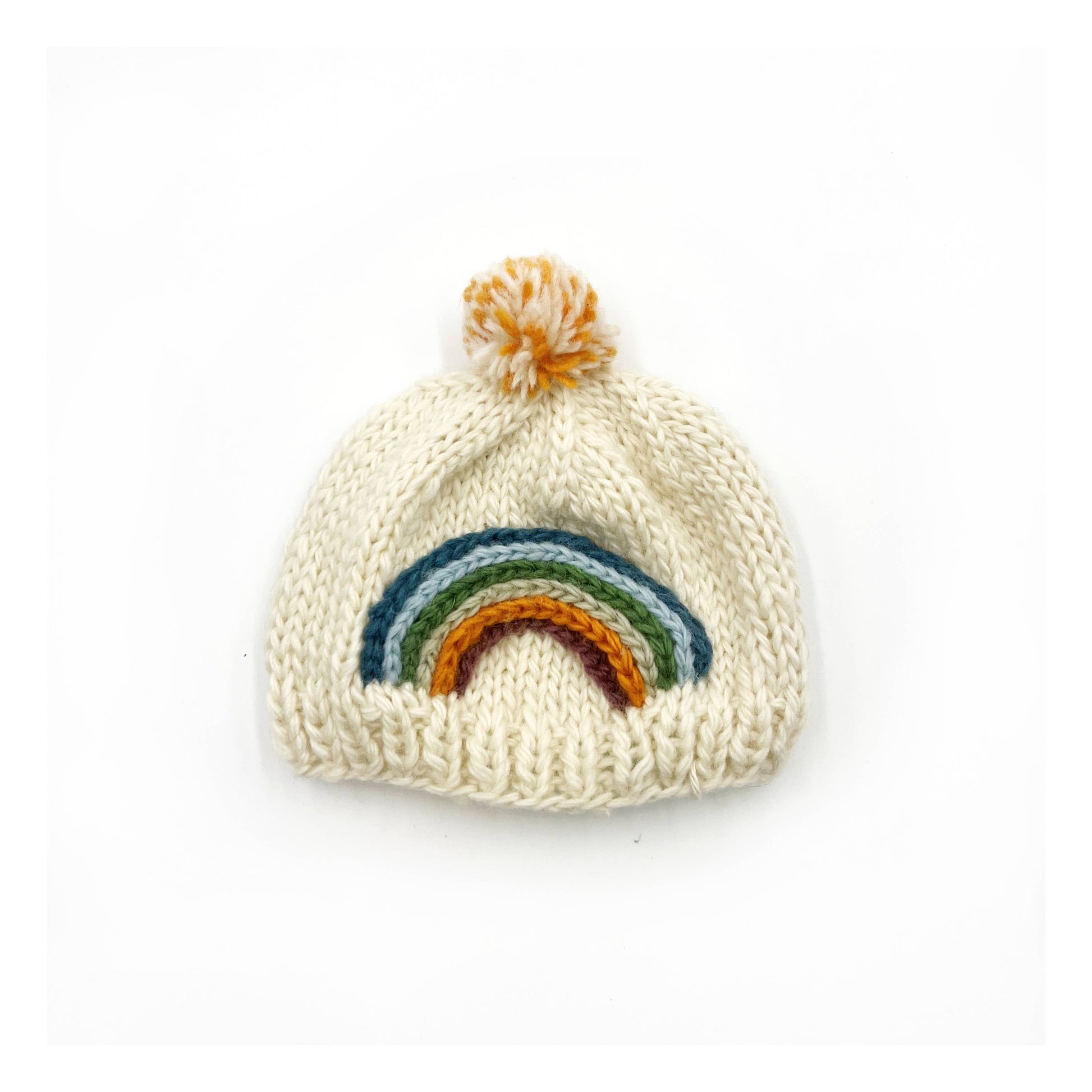 Thick, chunky woollen baby winter hat, by Pebble Child, made from 100% New Zealand merino wool in cream colour, with a knitted rainbow and a pompom on top.